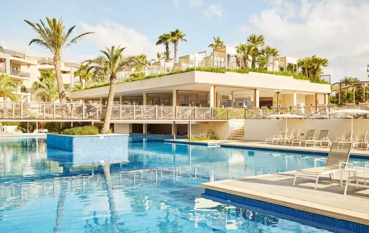 Piscina al aire libre con estructura elevada de palmeras y terraza con mobiliario en entorno natural en Mallorca