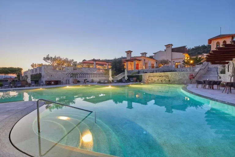 Piscina al aire libre con forma irregular y terraza pavimentada en entorno natural de Mallorca al atardecer