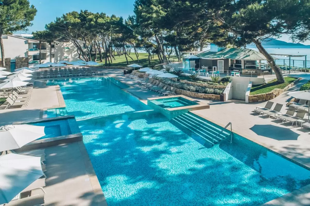 Piscina al aire libre con jacuzzi, tumbonas bajo sombrillas y vista al mar en Mallorca