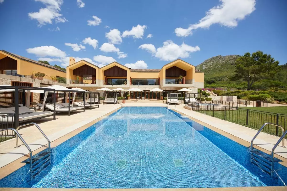 Piscina al aire libre con mosaico azul, camas de descanso con toldos y edificio moderno en Mallorca