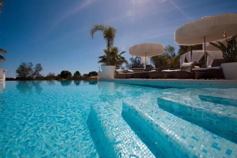 Piscina al aire libre con mosaicos azules, tumbonas con cojines y sombrillas blancas en Mallorca