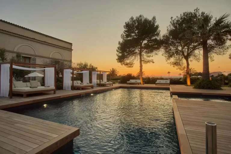 Piscina al aire libre con plataforma de madera y camas daybed en entorno natural al atardecer en Mallorca