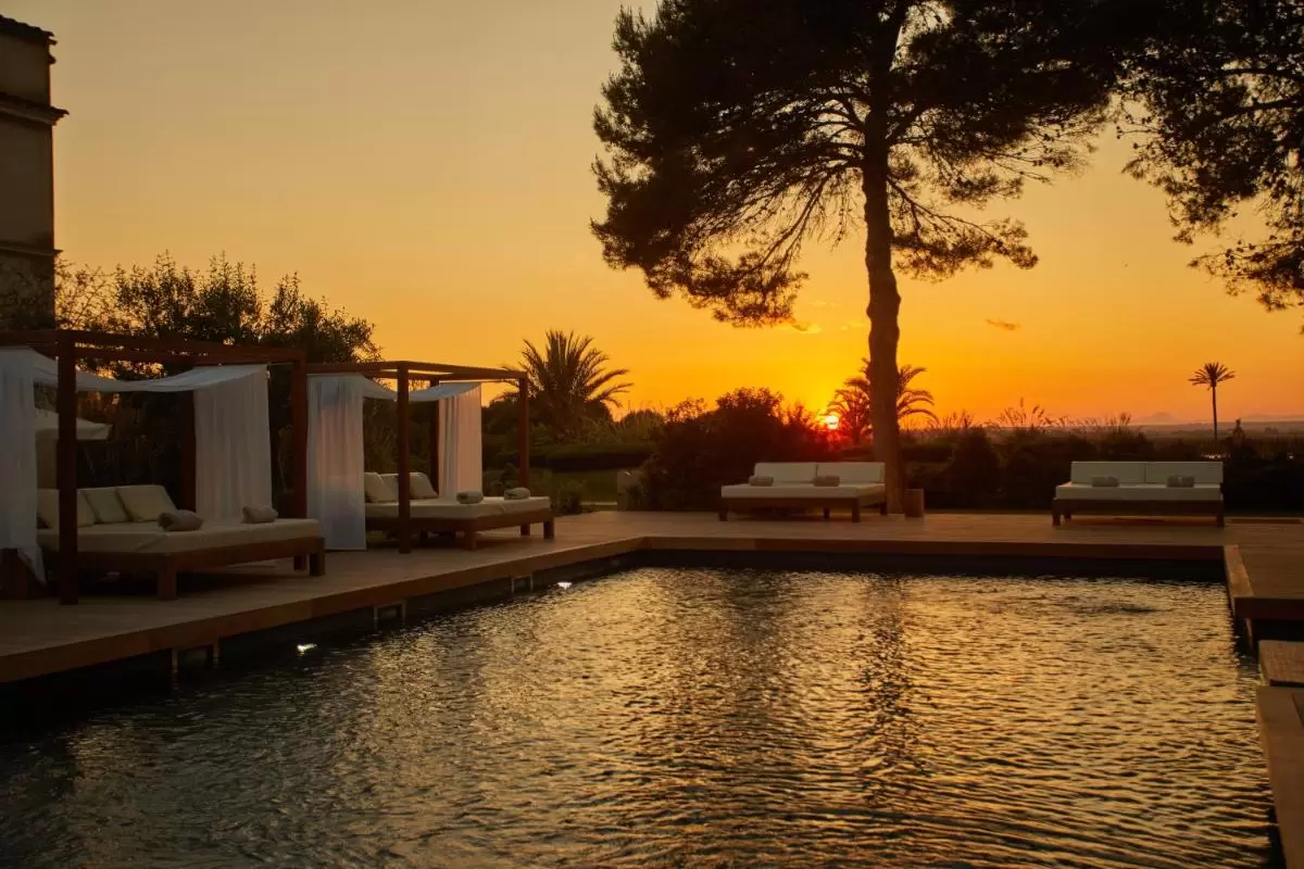 Piscina al aire libre con plataforma de madera y camastros bajo un atardecer en Mallorca