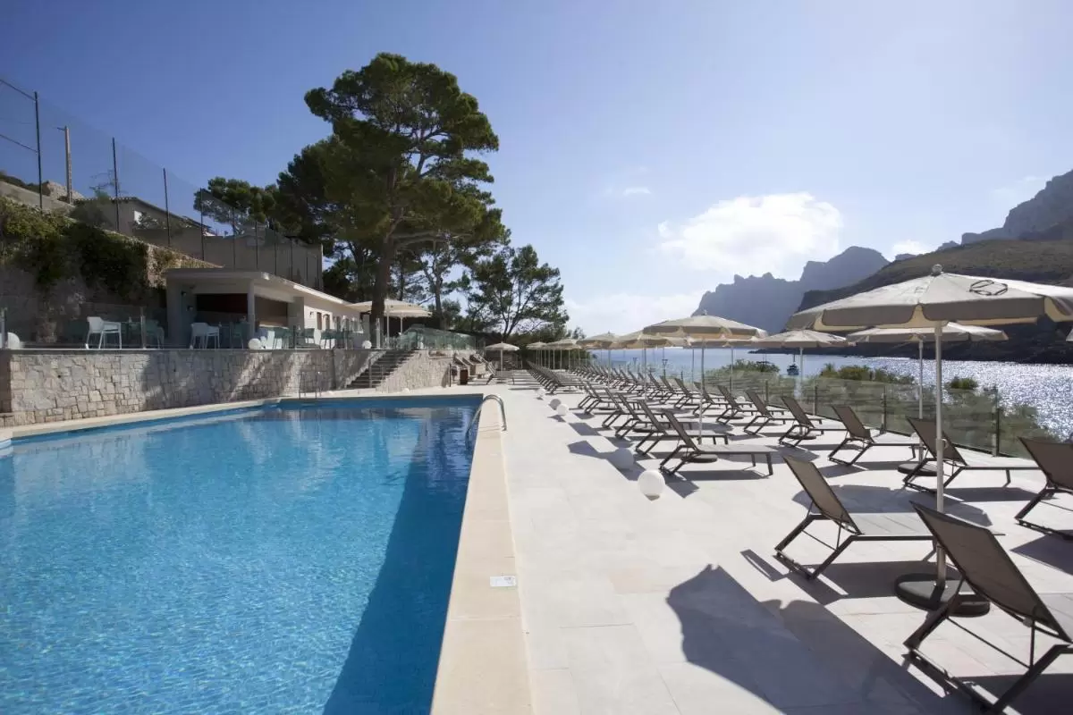 Piscina al aire libre con terraza, tumbonas y vistas panorámicas al mar y montañas en Mallorca