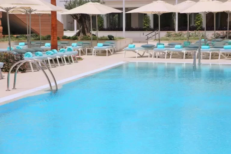 Piscina al aire libre con tumbonas blancas, sombrillas beige y entorno natural en Mallorca