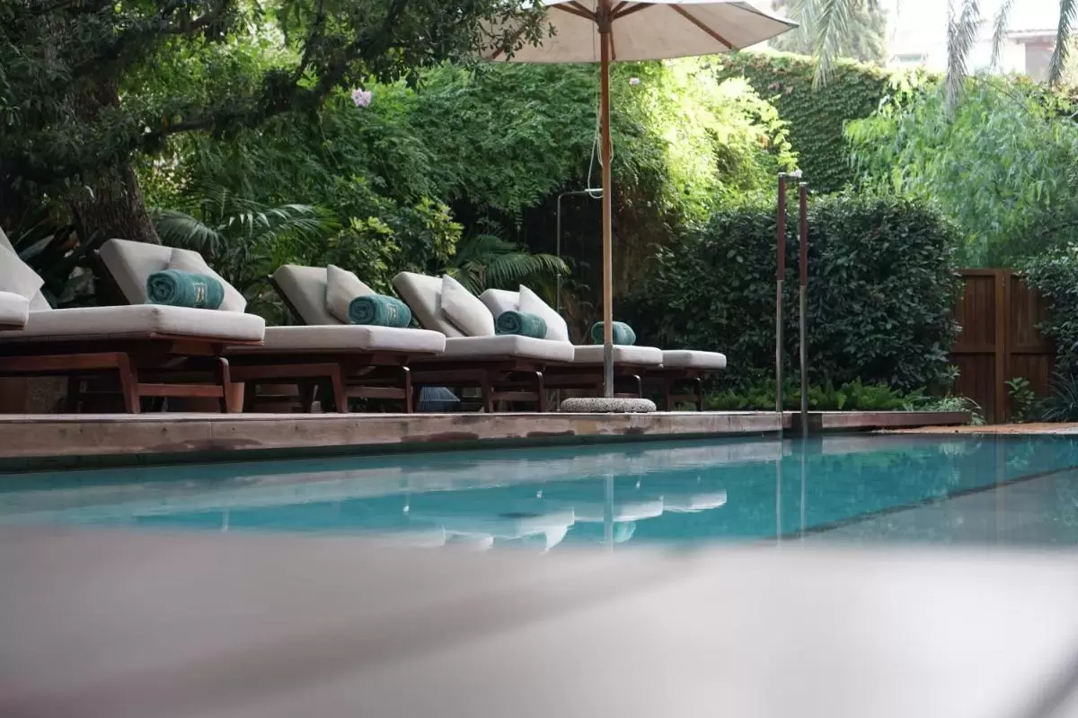 Piscina al aire libre con tumbonas, sombrilla blanca y vegetación en entorno natural en Mallorca