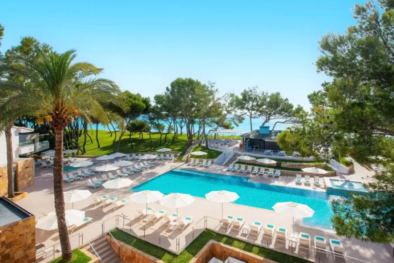 Piscina al aire libre con tumbonas turquesa y vistas al mar en entorno natural de Mallorca