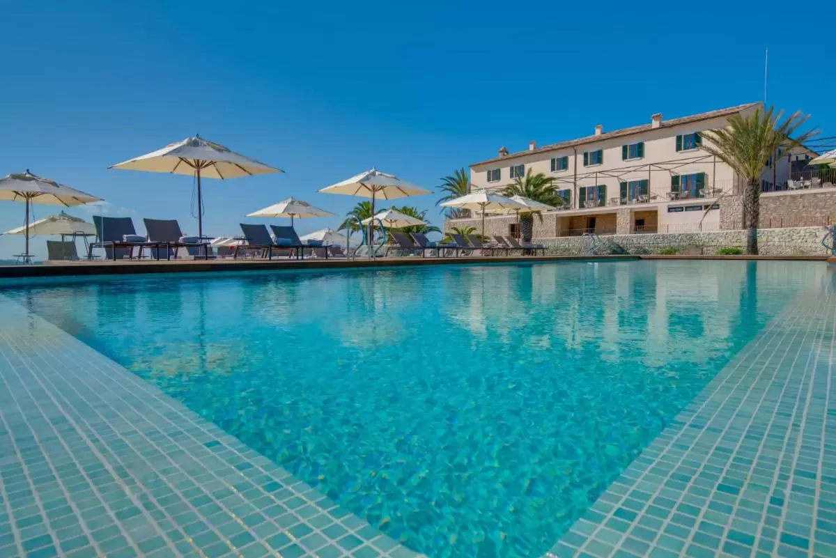 Piscina al aire libre con tumbonas y sombrillas blancas en entorno natural con palmeras en Mallorca