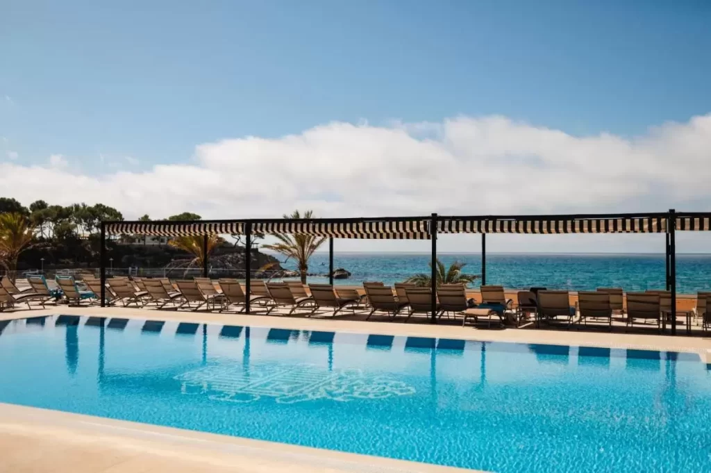 Piscina al aire libre con vistas al mar en Mallorca, rodeada de tumbonas y palmeras en ambiente costero tranquilo
