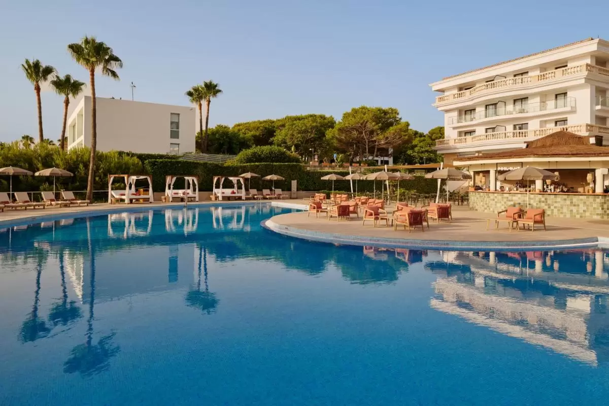 Piscina al aire libre con zona de descanso, camastros, palmeras y área techada en Mallorca al atardecer