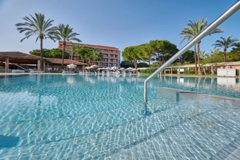 Piscina al aire libre en Mallorca con agua cristalina, sombrillas blancas y entorno natural de palmeras