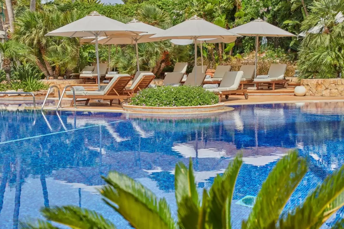 Piscina al aire libre en Mallorca con bordes redondeados, tumbonas de madera y vegetación tropical