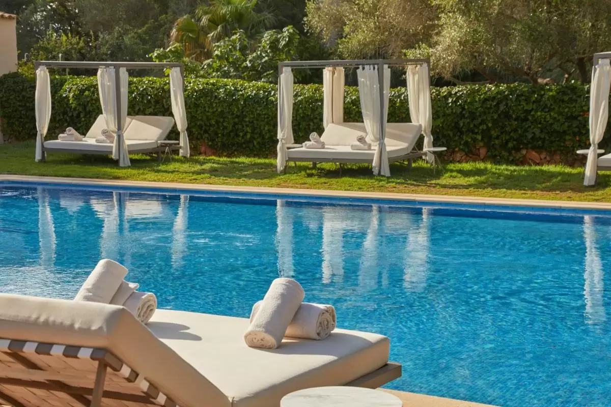 Piscina al aire libre en Mallorca con camas de descanso y entorno natural de césped y setos verdes