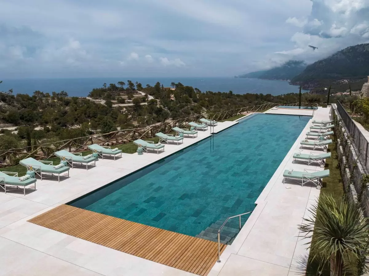 Piscina al aire libre en Mallorca con diseño moderno, tumbonas verdes y vistas a montañas y mar