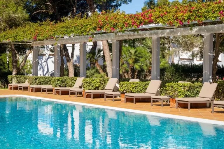 Piscina al aire libre en Mallorca con pérgola blanca, tumbonas beige y vegetación natural alrededor