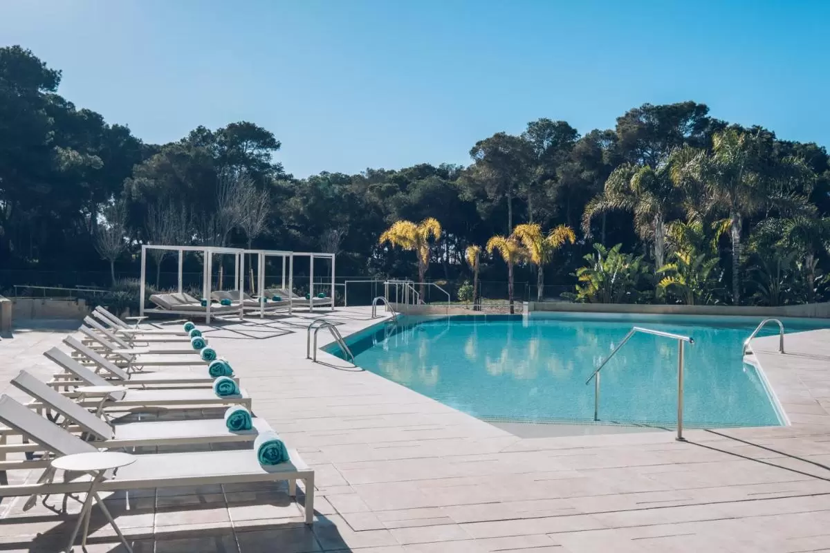 Piscina al aire libre en Mallorca con tumbonas blancas y entorno natural de coníferas y palmeras