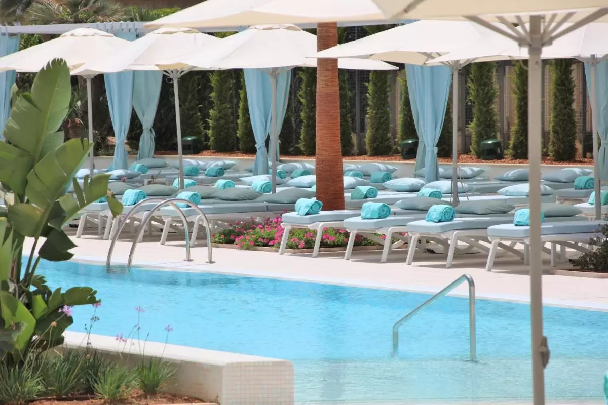 Piscina al aire libre en Mallorca con tumbonas turquesa, sombrillas blancas y pérgolas con cortinas azules
