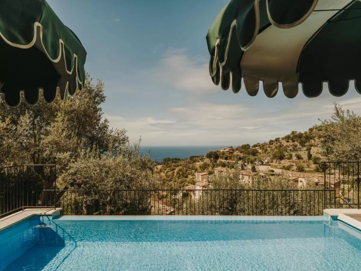 Piscina al aire libre en terraza elevada con toldos verdes y vistas a paisaje natural y masa de agua en Mallorca