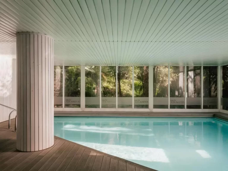 Piscina cubierta con agua clara y piso de madera oscura en espacio luminoso y natural en Mallorca