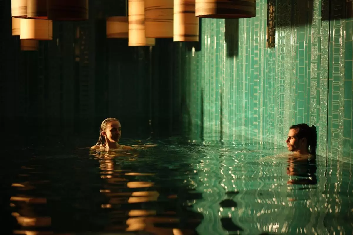 Piscina cubierta con azulejos verdes y luz cálida tenue, personas relajándose en ambiente tranquilo en Mallorca