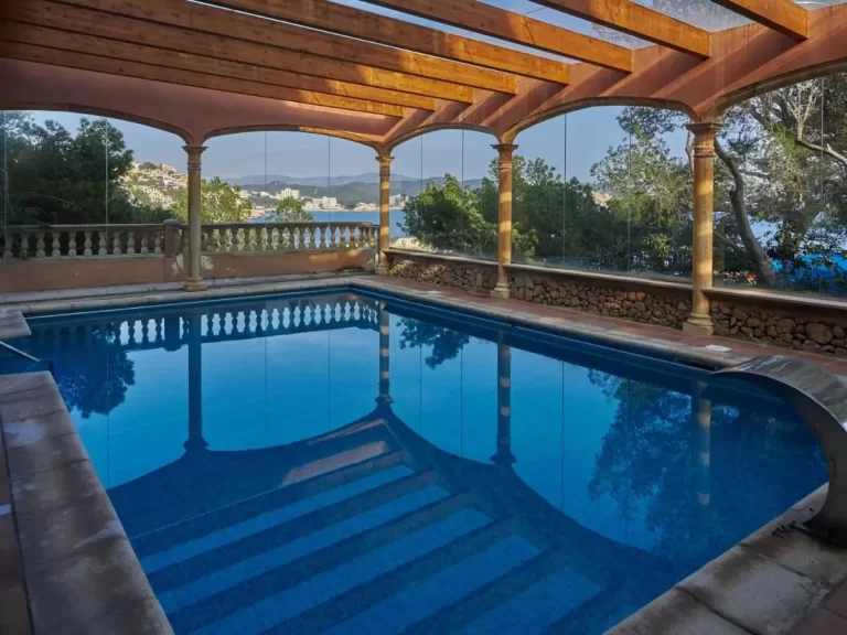 Piscina cubierta con estructura de vigas de madera y paredes de vidrio en entorno natural de Mallorca