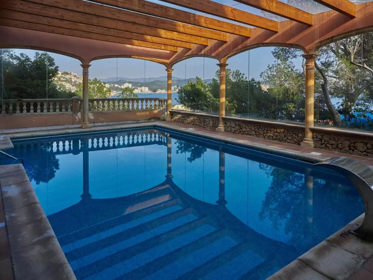 Piscina cubierta con estructura de vigas de madera y paredes de vidrio en entorno natural de Mallorca