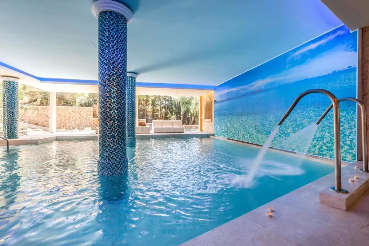 Piscina cubierta moderna en Mallorca con chorros de agua, columnas de mosaico y mural marino relajante