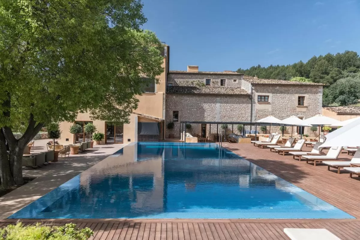 Piscina de borde infinito con deck de madera, tumbonas y zona lounge en entorno natural en Mallorca