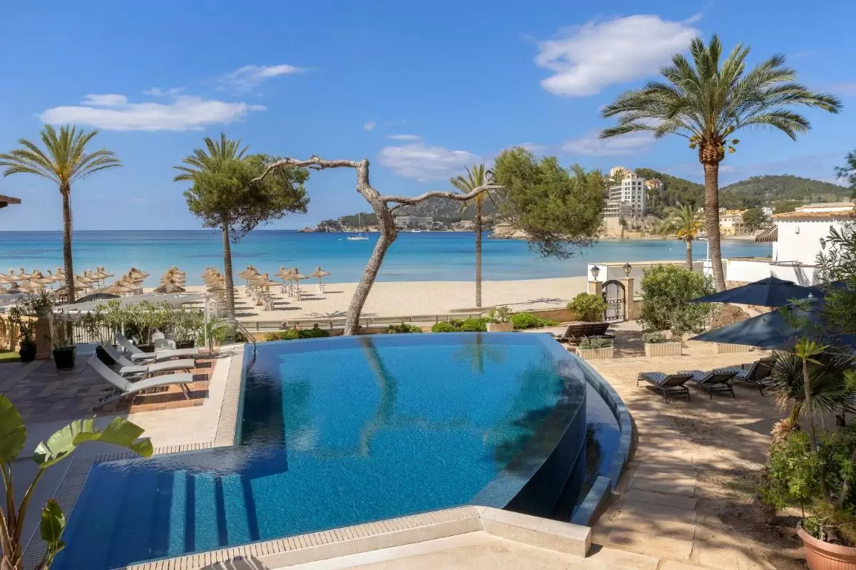 Piscina de borde infinito con vistas al mar turquesa y playa de arena clara en Mallorca