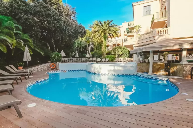 Piscina exterior con diseño irregular, borde decorativo azul y área de descanso con tumbonas y sombrillas en Mallorca