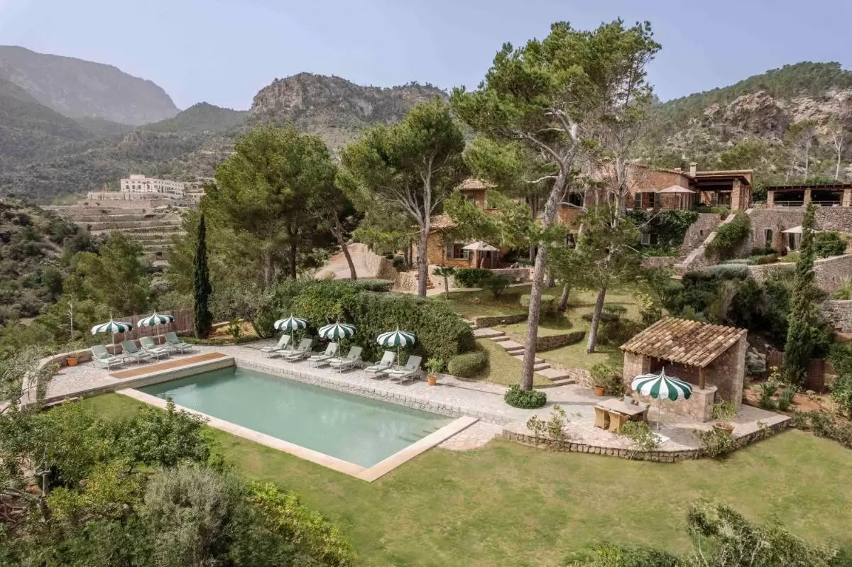 Piscina exterior con tumbonas y sombrillas verdes en entorno natural montañoso de Mallorca