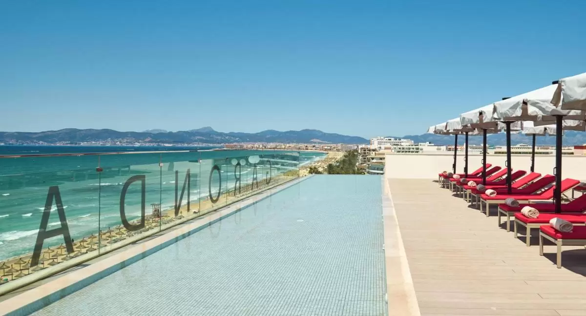 Piscina infinita con vistas al mar en terraza elevada con tumbonas rojas y sombrillas blancas en Mallorca