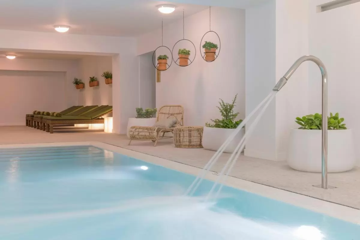HM Ayron Park - Adults Only Piscina interior con chorros de agua, tumbonas con toallas verdes y decoración natural en Mallorca