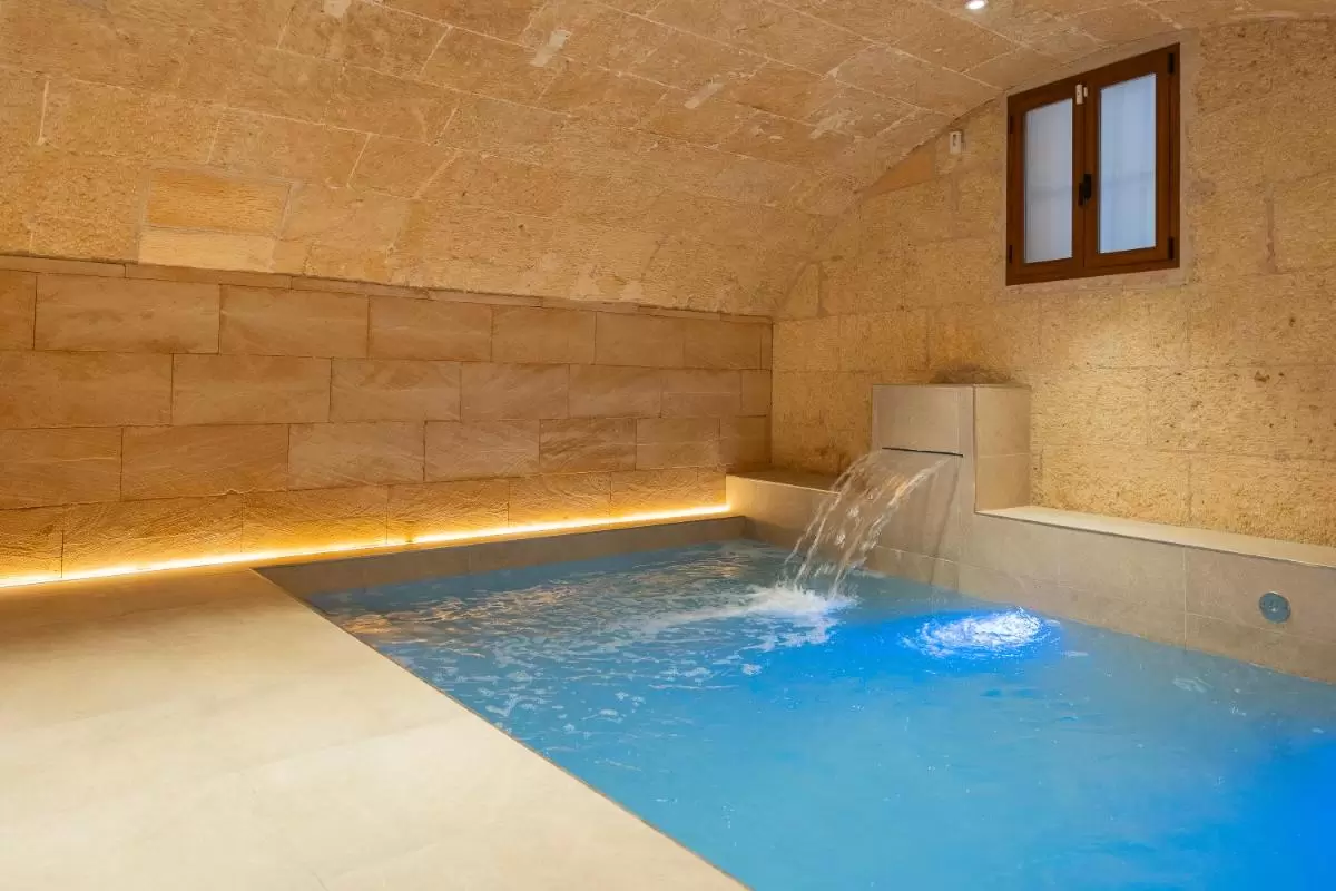 Piscina interior con iluminación LED azul y diseño en piedra natural estilo spa en Mallorca