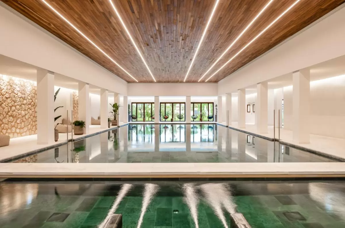 Piscina interior moderna con jacuzzi, iluminación LED y vistas a jardín natural en Mallorca