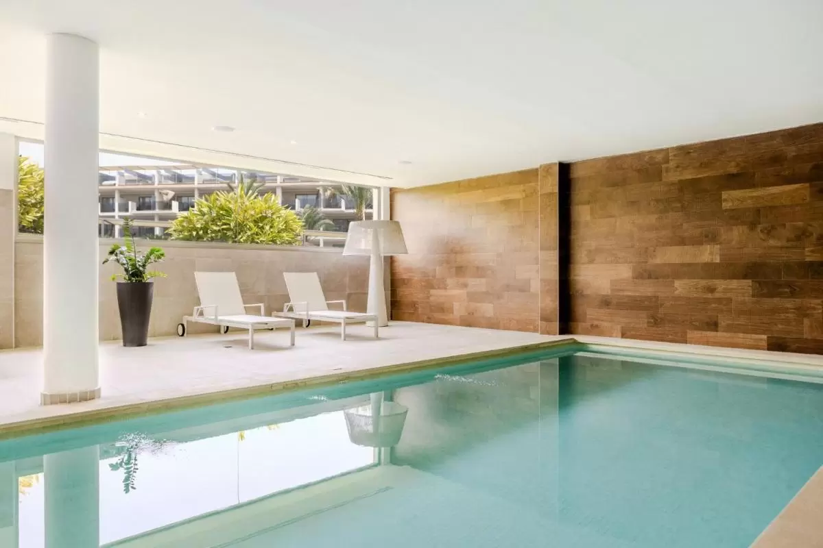 Piscina interior moderna con jacuzzi, tumbonas blancas y diseño minimalista en Mallorca