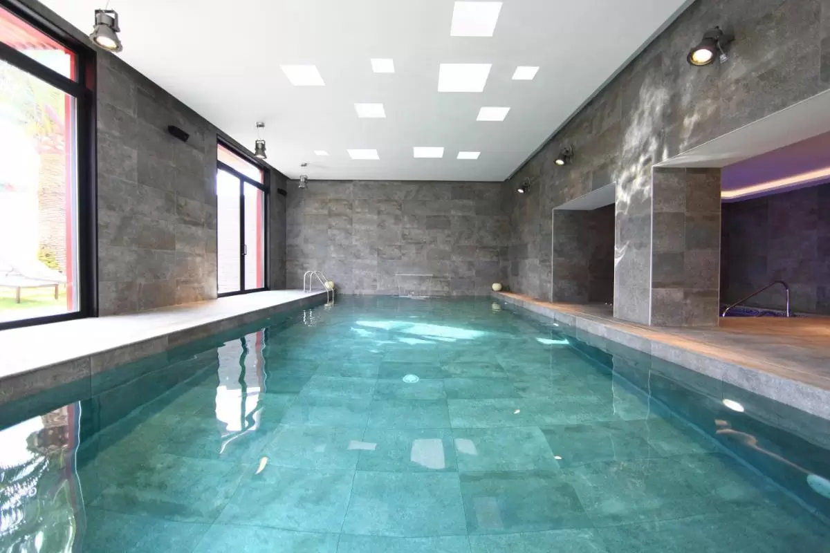 Piscina interior moderna en Mallorca con azulejos azul verdoso y paredes de tono gris oscuro minimalista