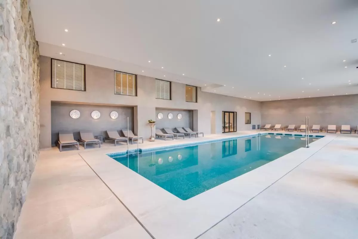 Piscina interior moderna en Mallorca con diseño minimalista, luz natural y área de descanso con tumbonas