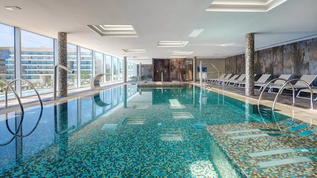 Piscina interior moderna en Mallorca con mosaicos, jacuzzi integrado y amplios ventanales para luz natural