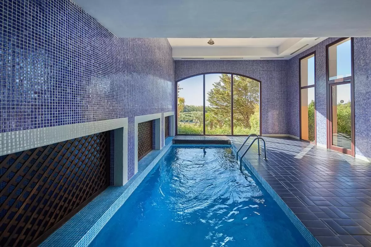 Pula Suites Boutique Resort Piscina interior rectangular con azulejos azules y blancos, iluminación natural y acceso con escalera metálica en Mallorca