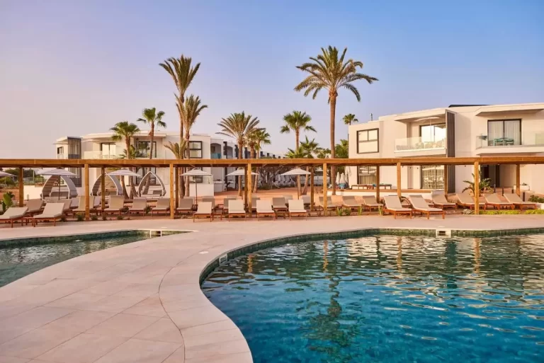 Piscina irregular con pérgola, tumbonas y vegetación en entorno moderno de Mallorca al atardecer