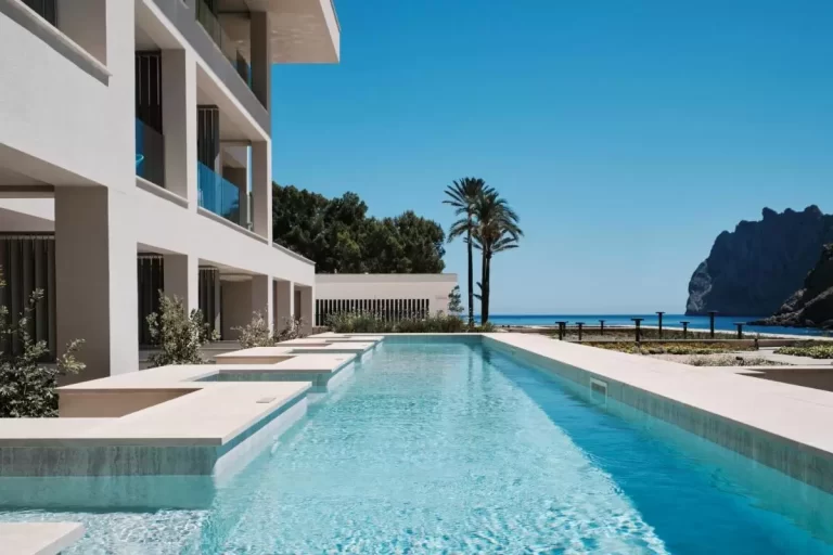 Piscina rectangular al aire libre con agua cristalina junto a edificio moderno y vistas al mar en Mallorca