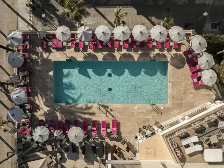 Piscina rectangular al aire libre con tumbonas rosas y sombrillas blancas en entorno soleado de Mallorca