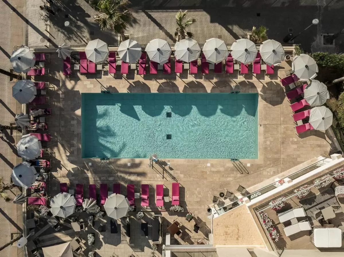 Piscina rectangular al aire libre con tumbonas rosas y sombrillas blancas en entorno soleado de Mallorca