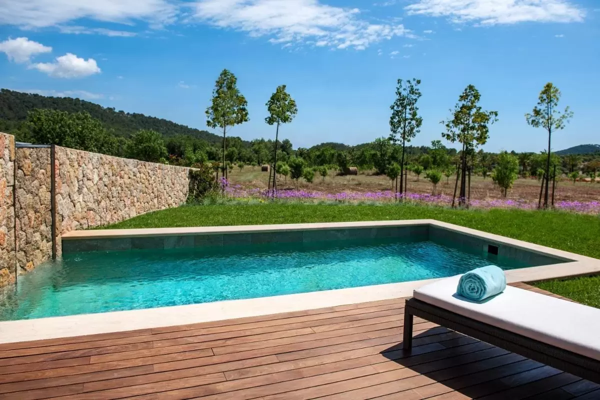 Piscina rectangular con borde de piedra y tumbona en entorno natural de Mallorca con vistas a colinas verdes