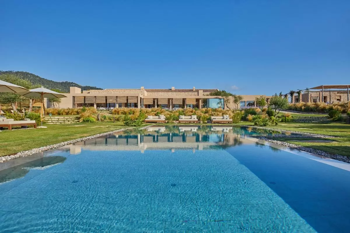 Piscina rectangular con bordes de piedra y área de césped en entorno natural de Mallorca con mobiliario exterior y pérgola