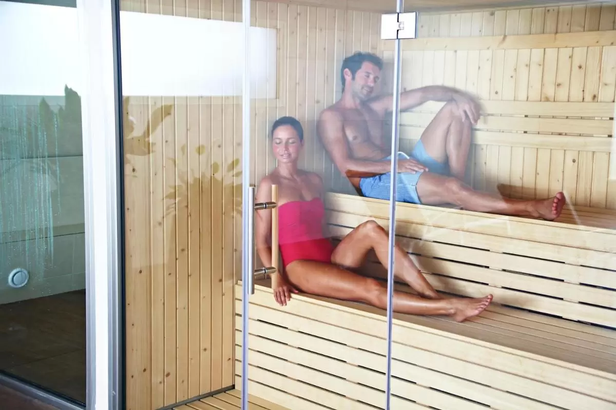Relajación en sauna de madera clara con diseño de bancos escalonados y puerta de vidrio en Mallorca