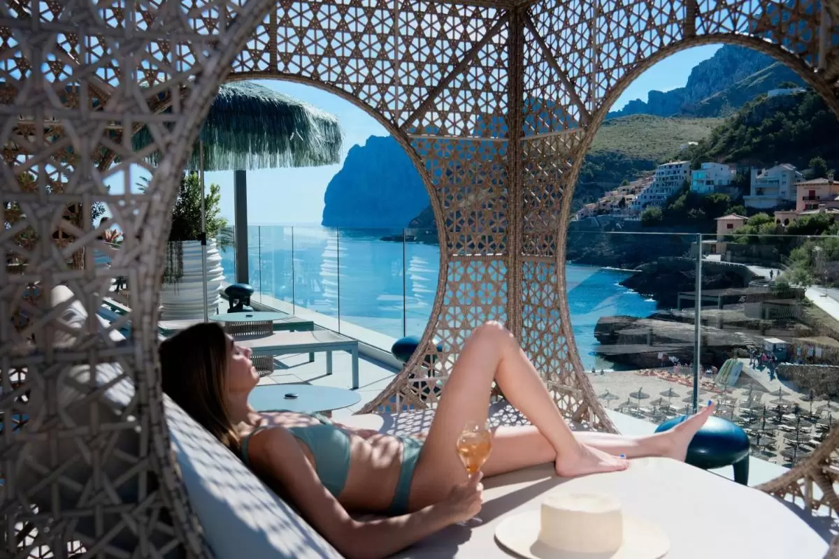 Relajación en terraza con tumbona de mimbre y vista panorámica al mar y montañas en Mallorca