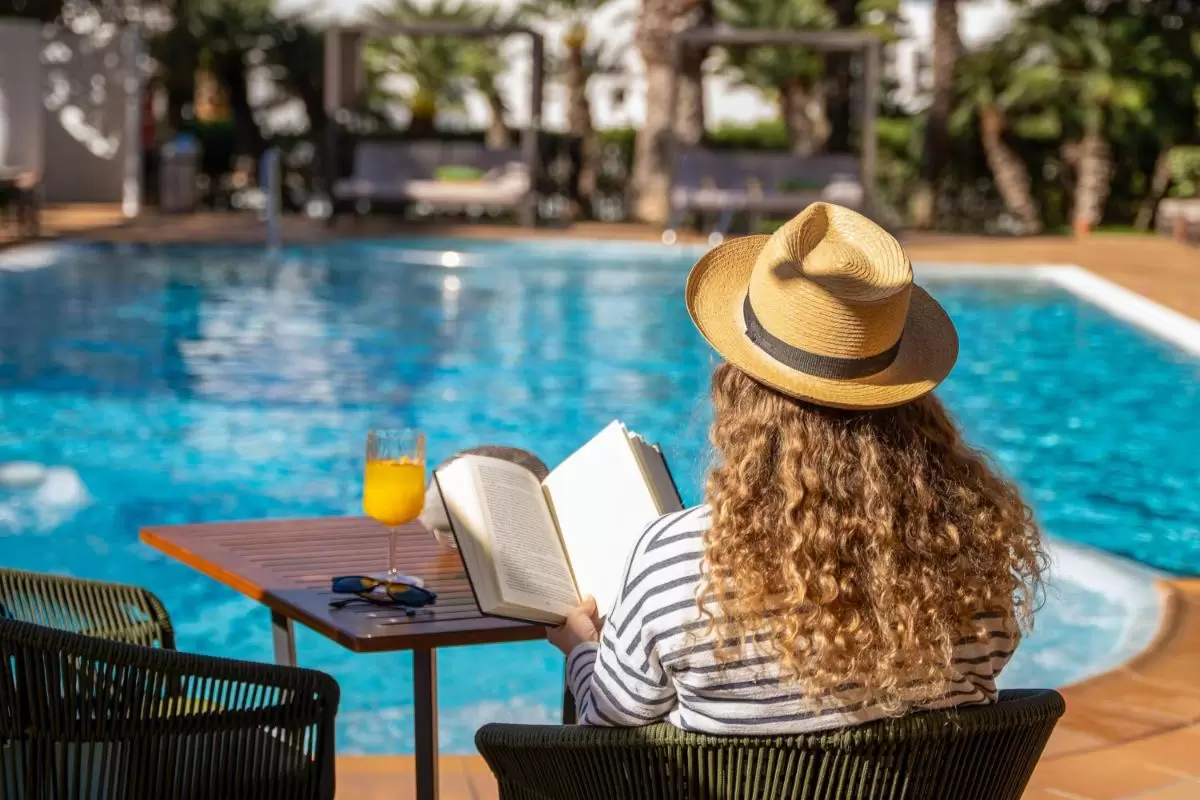 Relajación junto a piscina al aire libre con lectura, bebida y ambiente natural en Mallorca soleada