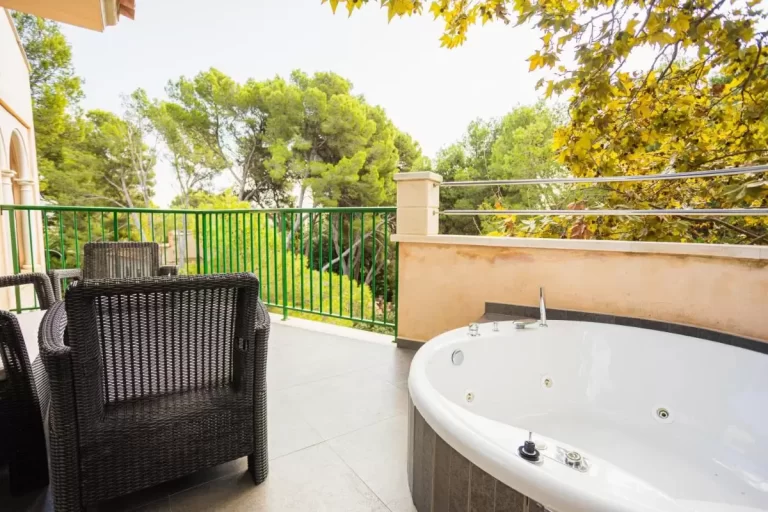 Terraza al aire libre con bañera de hidromasaje ovalada y sillas de mimbre en entorno natural en Mallorca